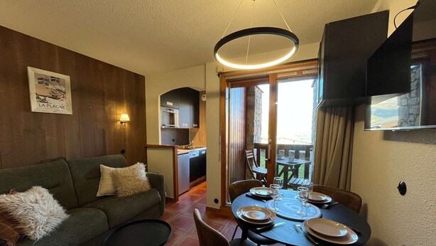 A cozy living area with a sofa, a dining table set for two, and a kitchen in the background. - Newly renovated slopeside studio (Montchavin-les-coches)