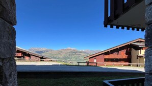 A view of a mountain lodge with a clear sky, featuring a gravel driveway and a stone wall. - Newly renovated slopeside studio (Montchavin-les-coches)