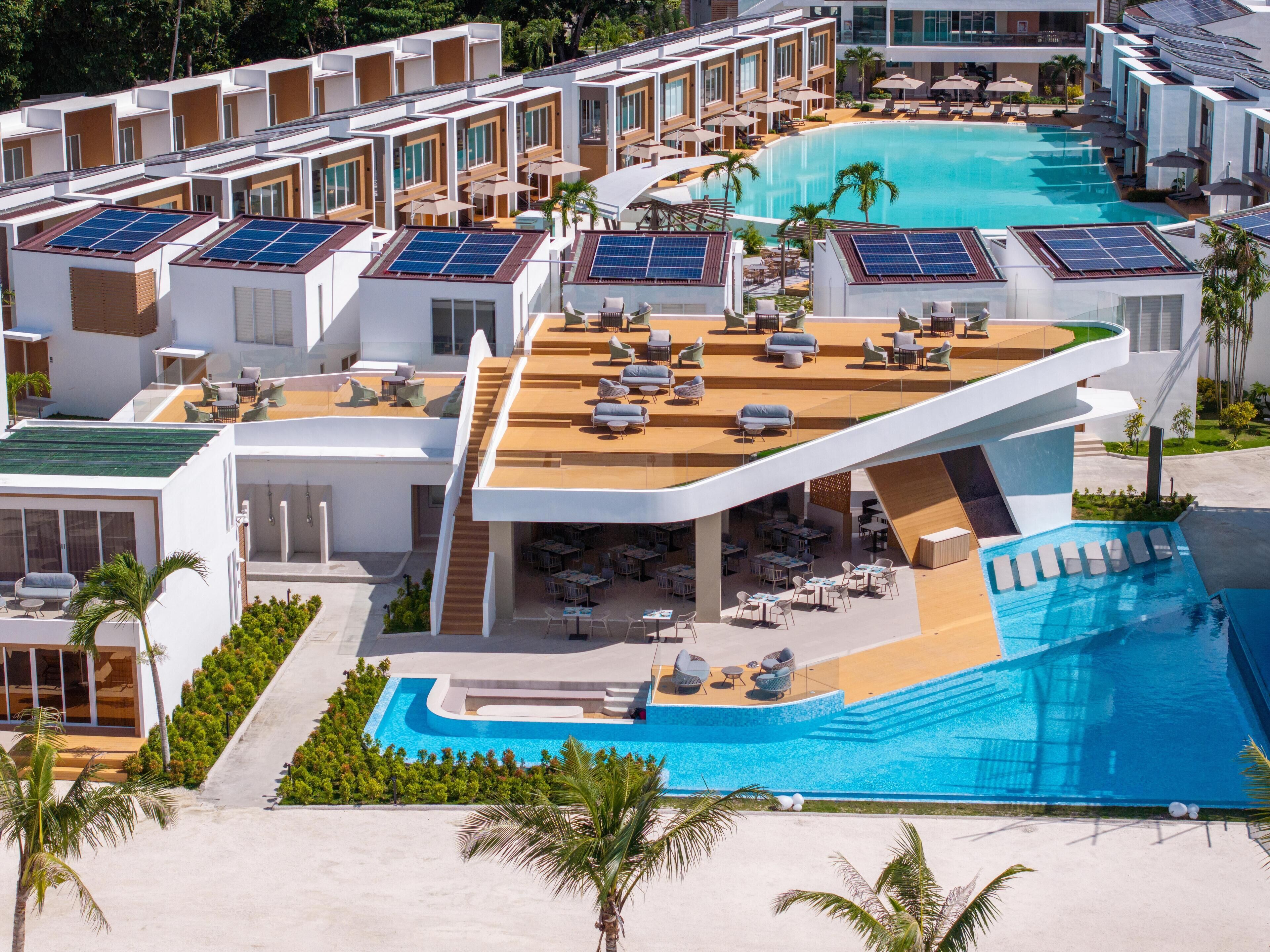 Un hotel moderno con piscina en la azotea, paneles solares y espacios de estar al aire libre.