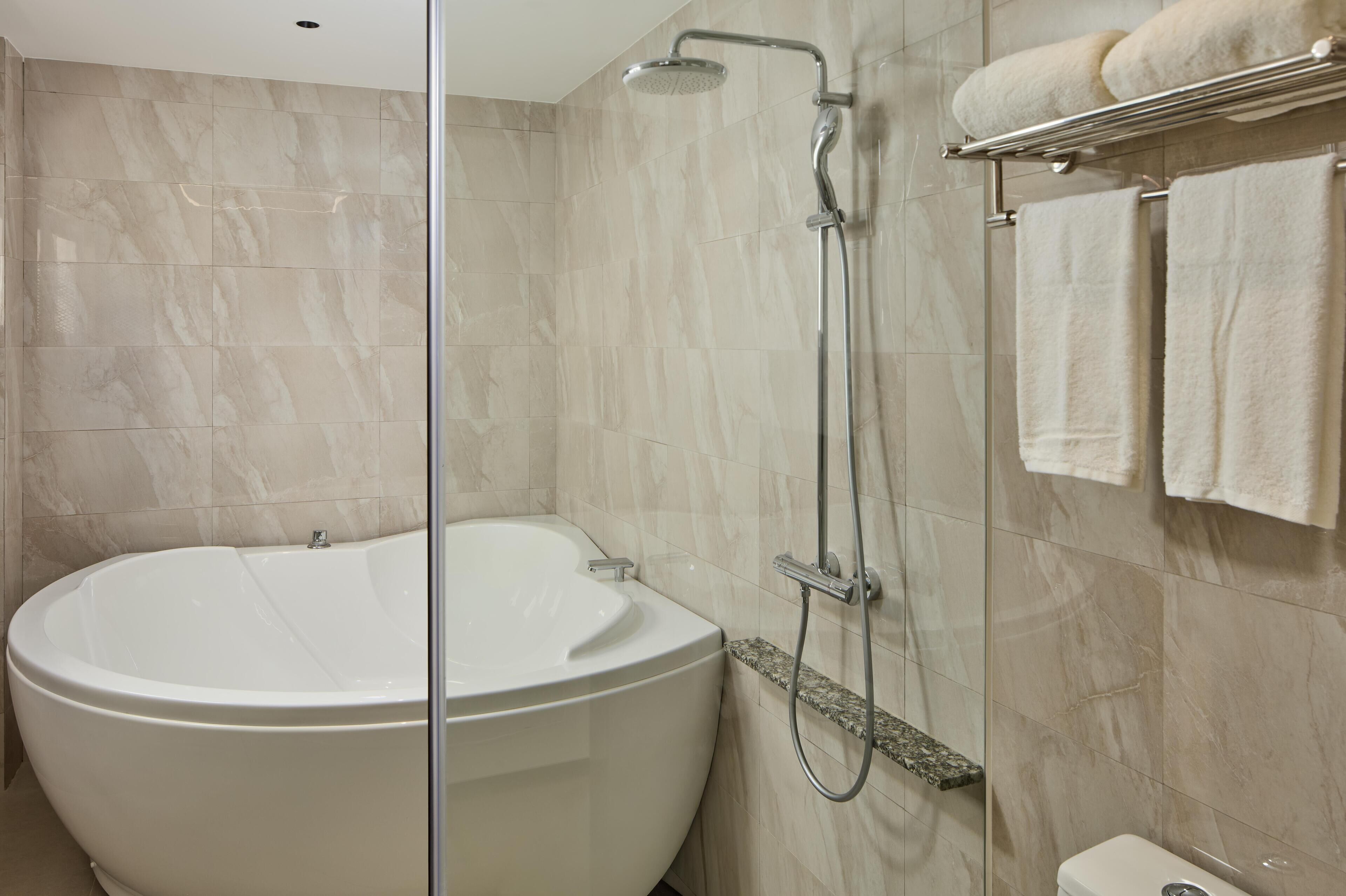 A modern bathroom with a freestanding bathtub, a glass-enclosed shower, and a towel rack with multiple towels.