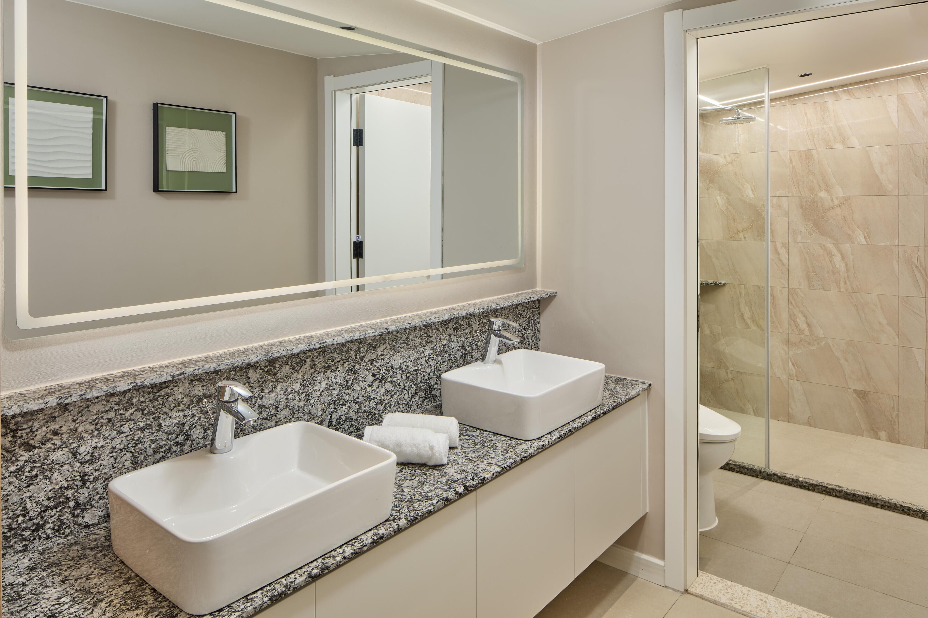 A modern bathroom with two sinks, a large mirror, and a shower area.