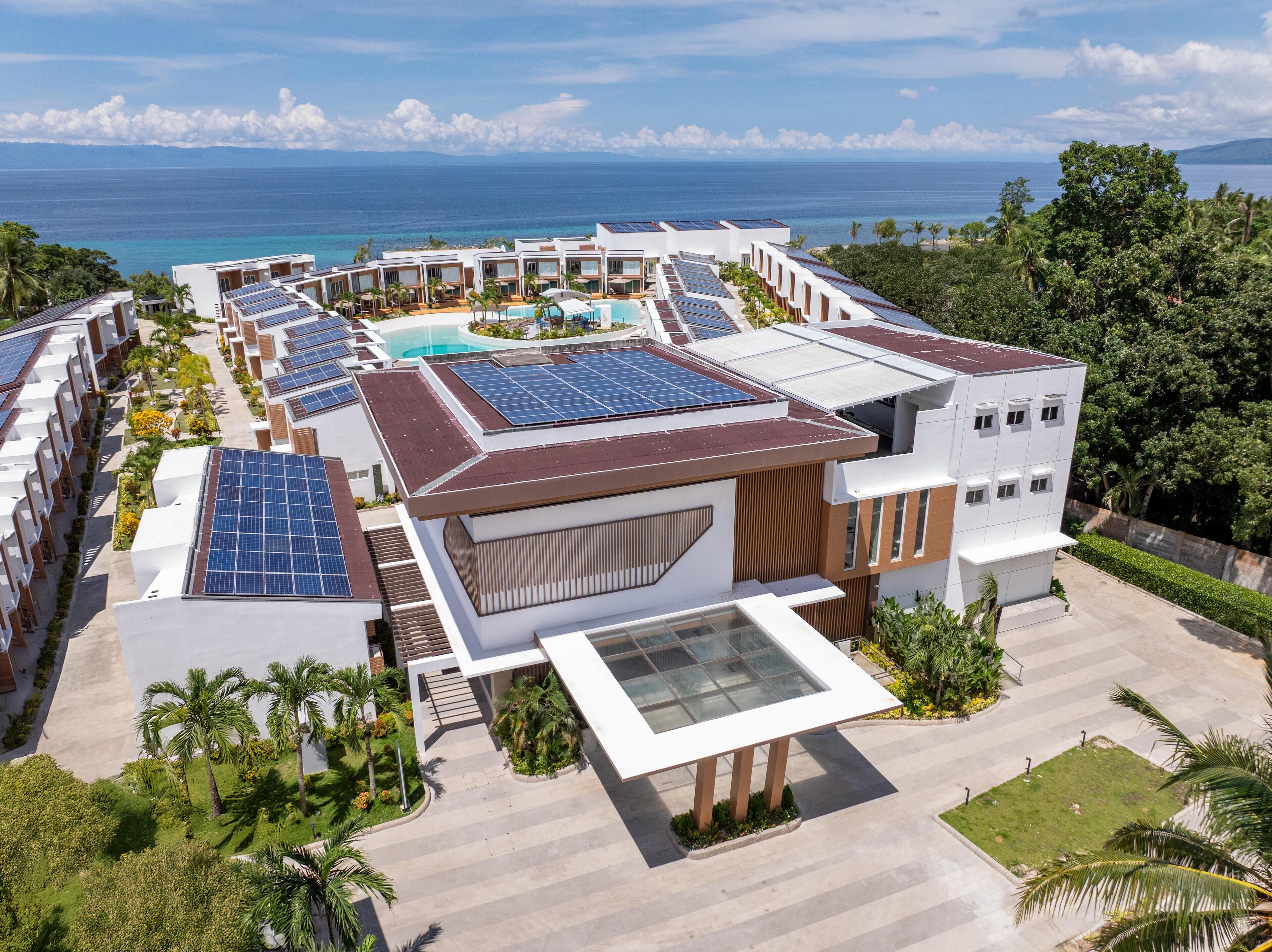 A resort with multiple buildings, solar panels, a swimming pool, and a view of the ocean.