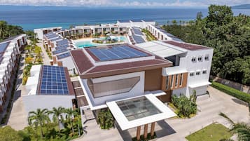 A resort with multiple buildings, solar panels, a swimming pool, and a view of the ocean.