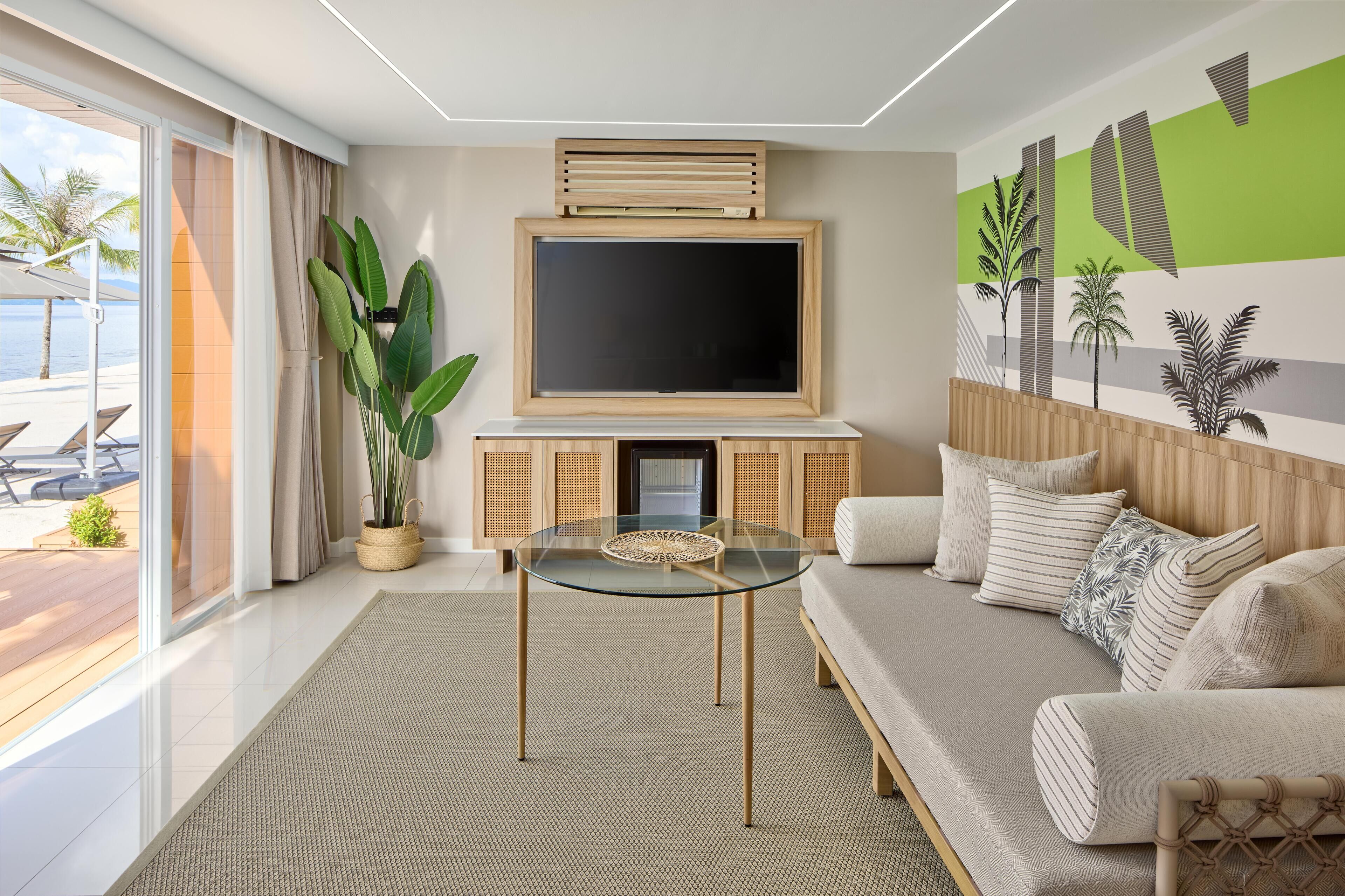 Uma sala de estar moderna com uma mesa de centro de vidro, sofá, televisão de tela plana e uma grande planta em vaso.