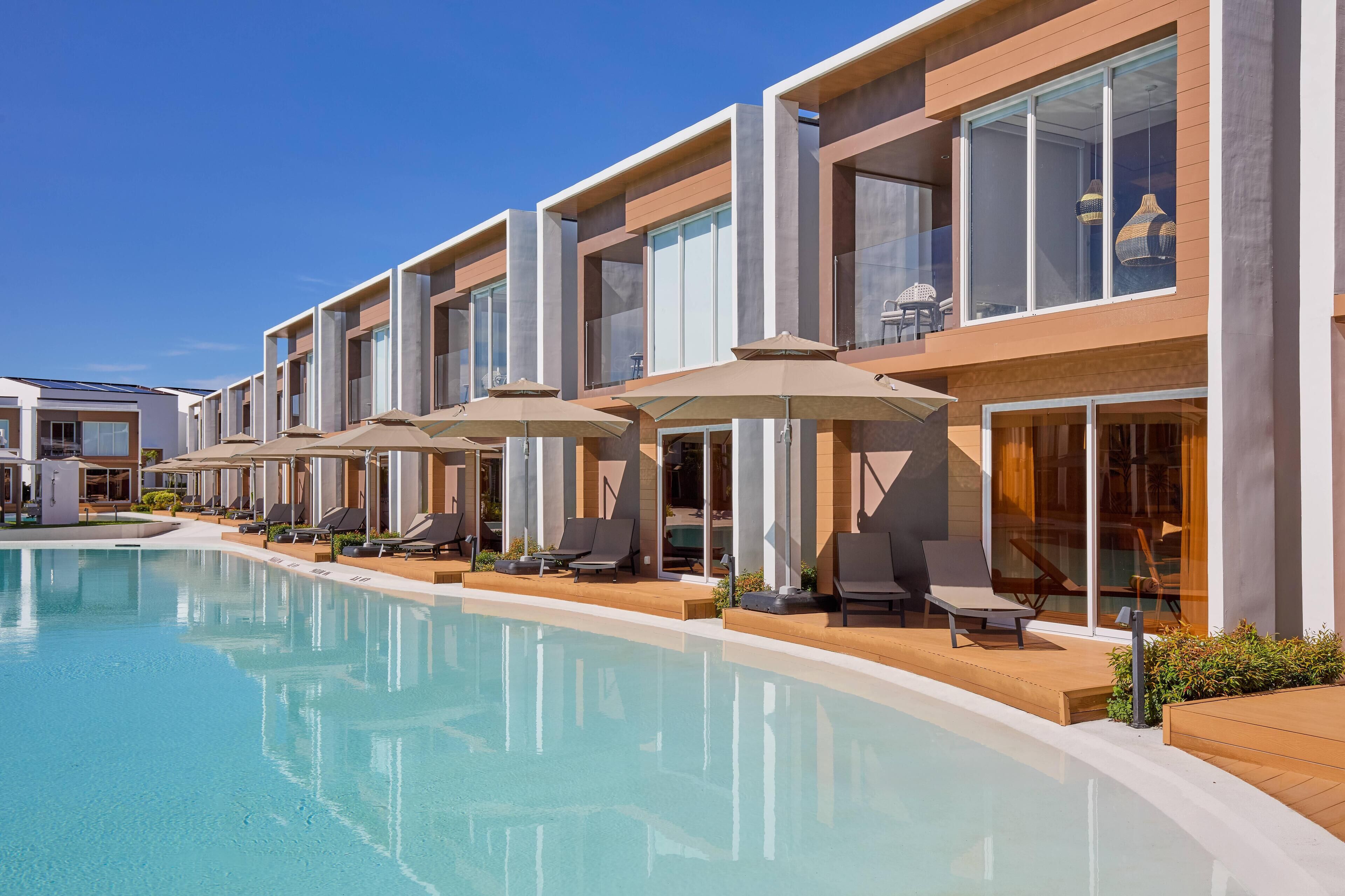 Un hôtel moderne doté d’une piscine, de chaises longues et de parasols.