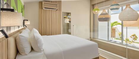 A modern hotel room with a large bed, a view of the city, and a large window with hanging lights.