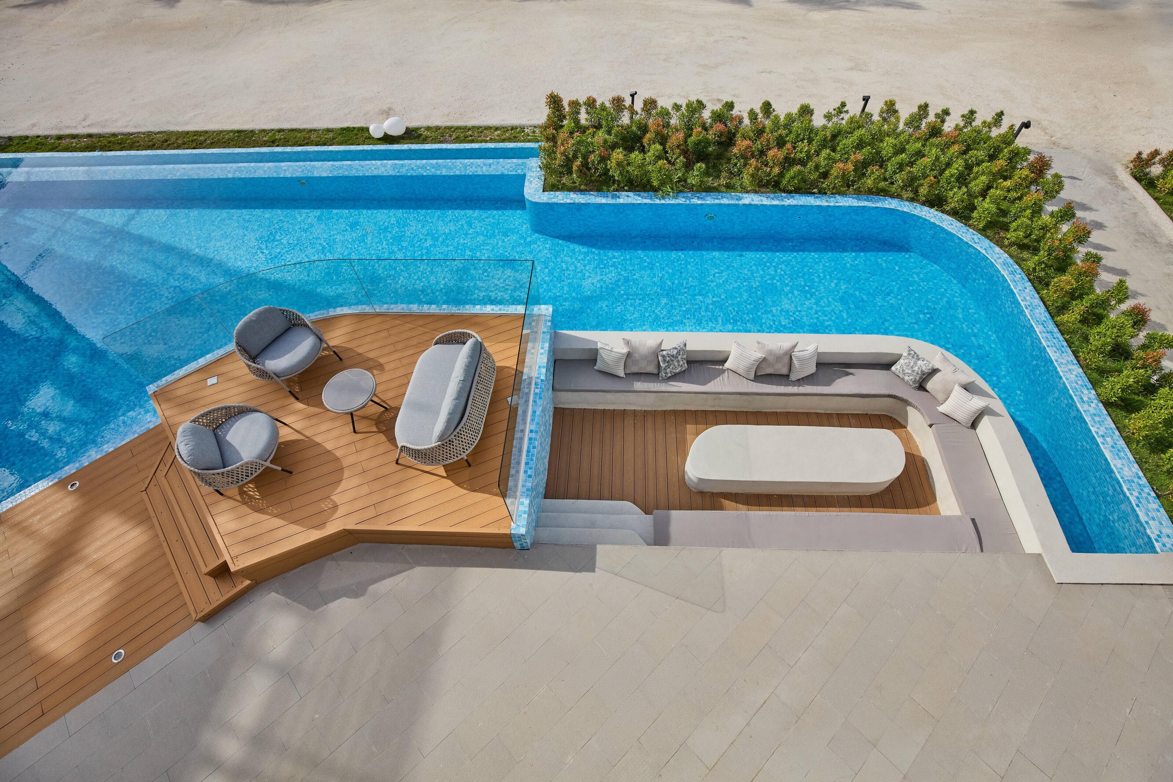 Una piscina con muelle de madera, sillas de descanso y zona de estar.