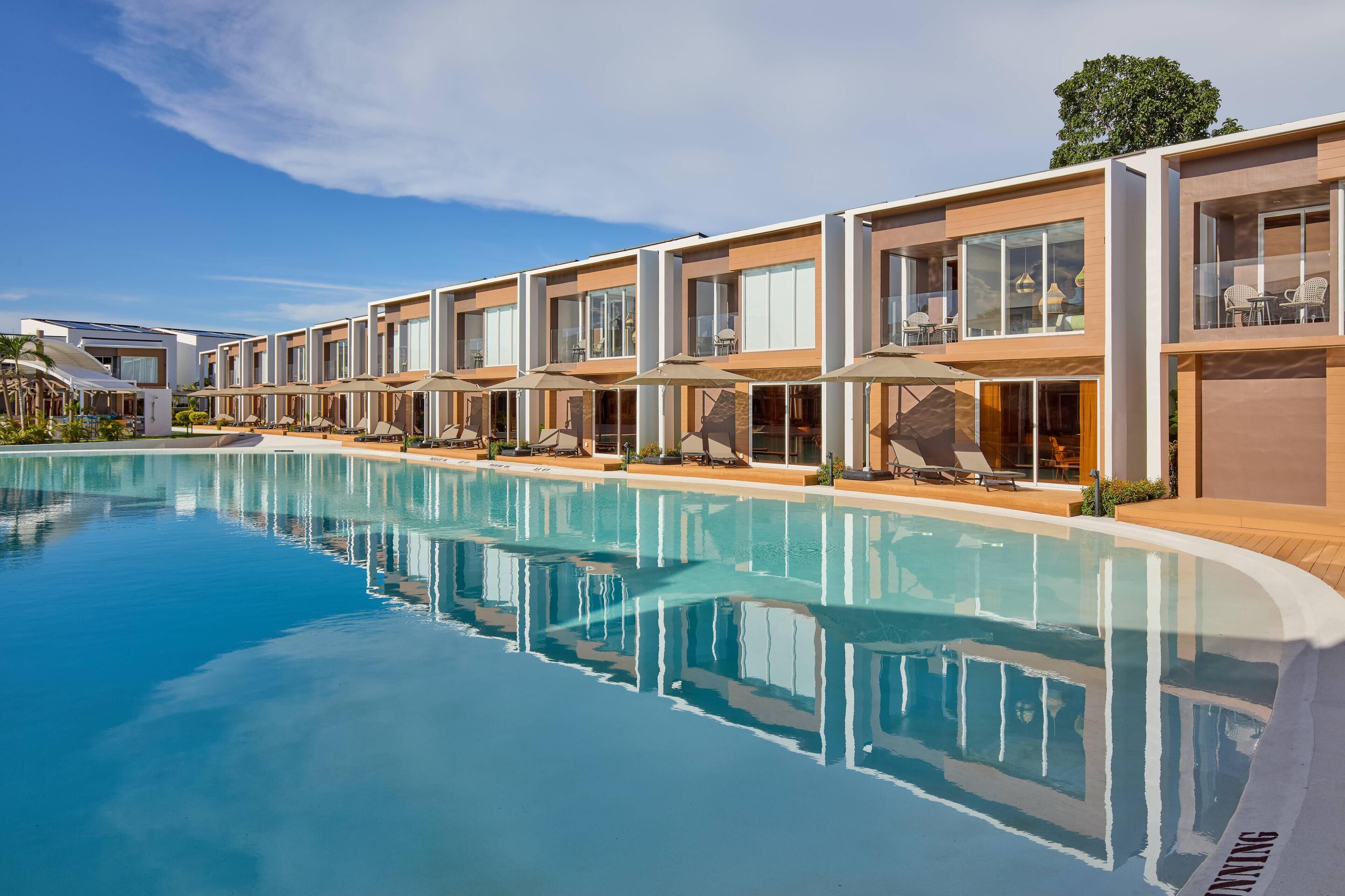 A modern hotel with a swimming pool, outdoor seating, and a clear blue sky.