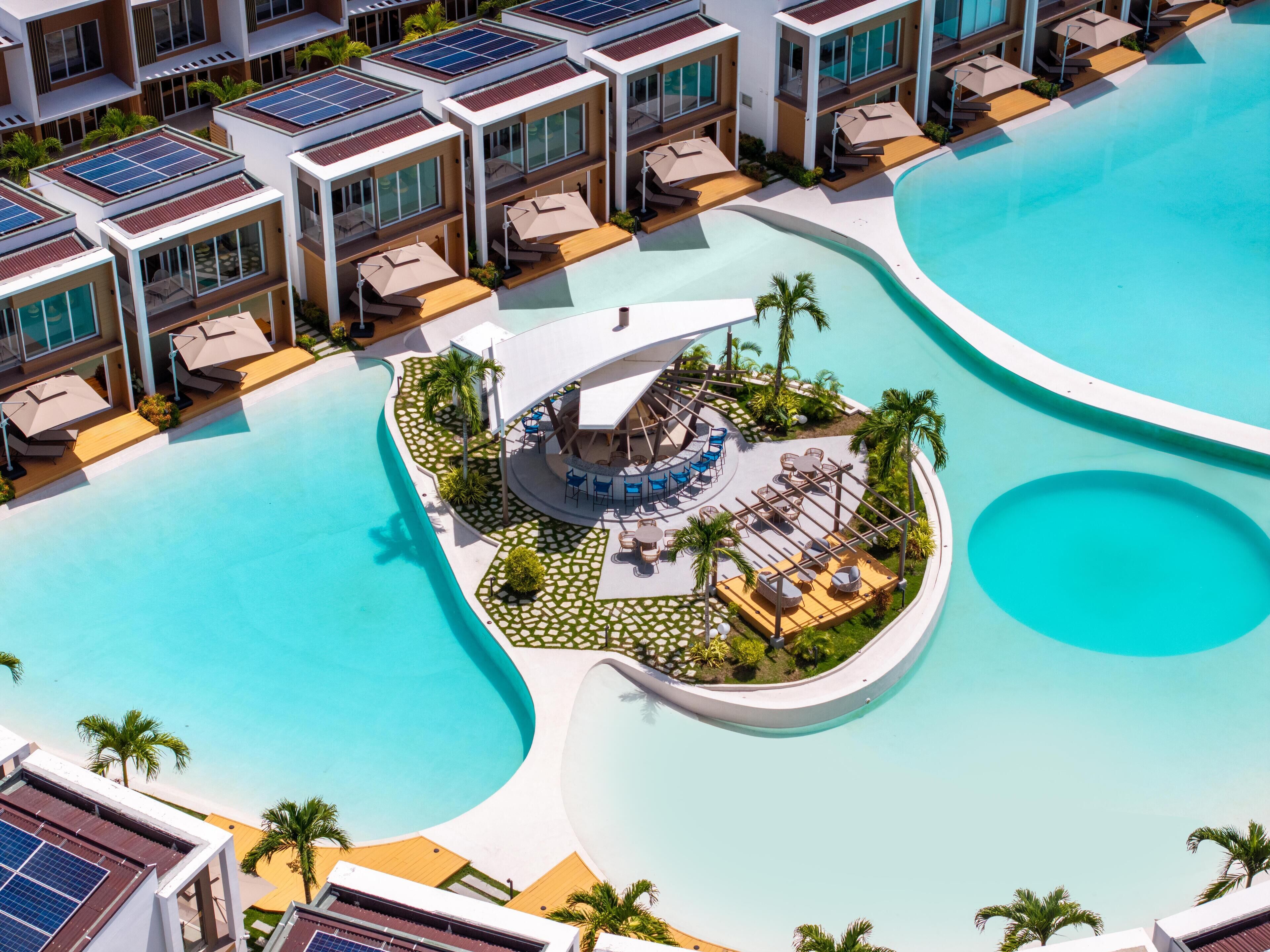 Ein modernes Resort mit einem zentralen Poolbereich, mehreren Gästezimmern mit Balkonen und Solaranlagen auf den Dächern.