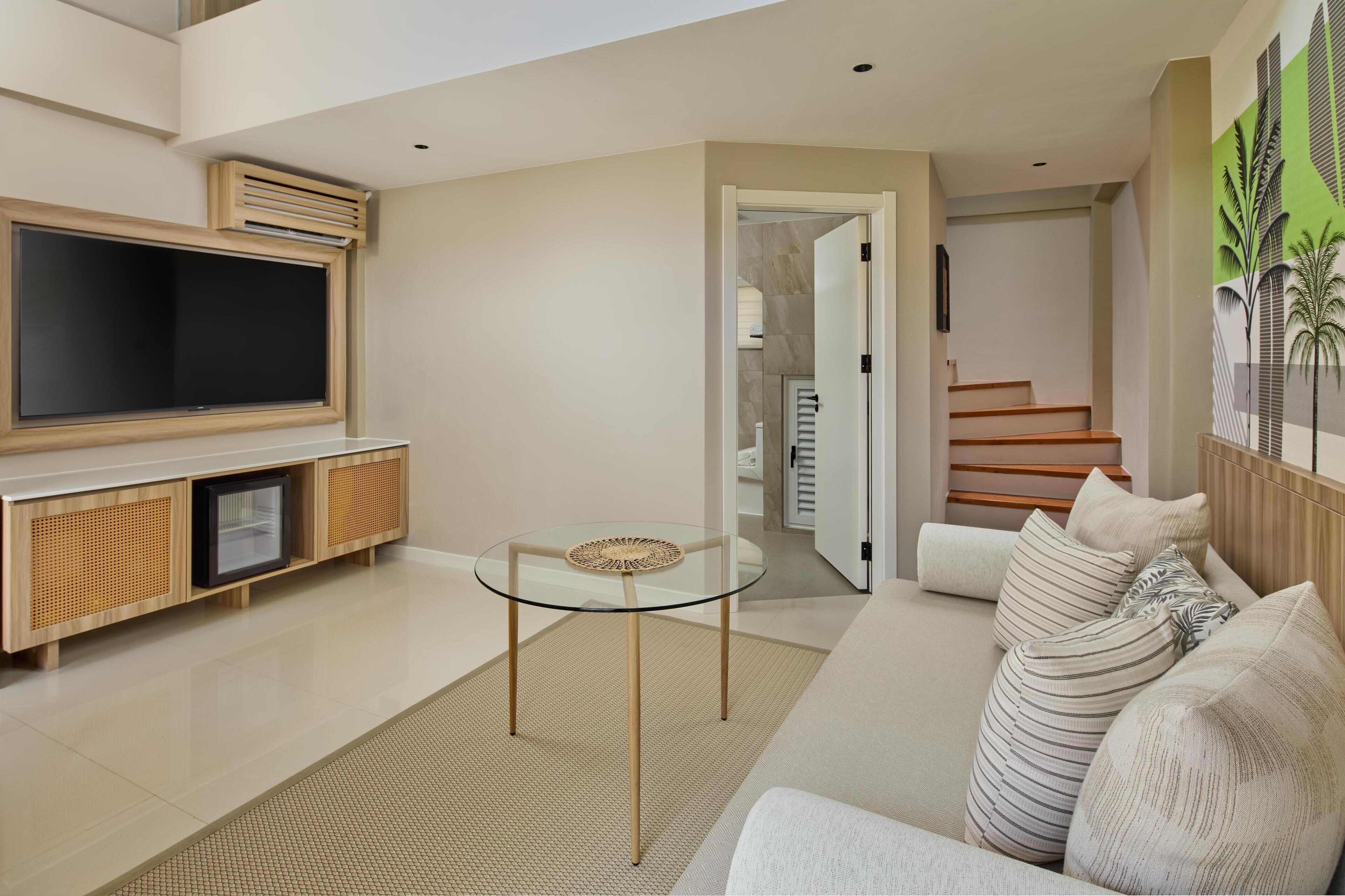 A modern living room with a flat-screen TV, a glass coffee table, a sofa with striped cushions, and a staircase leading to another level.