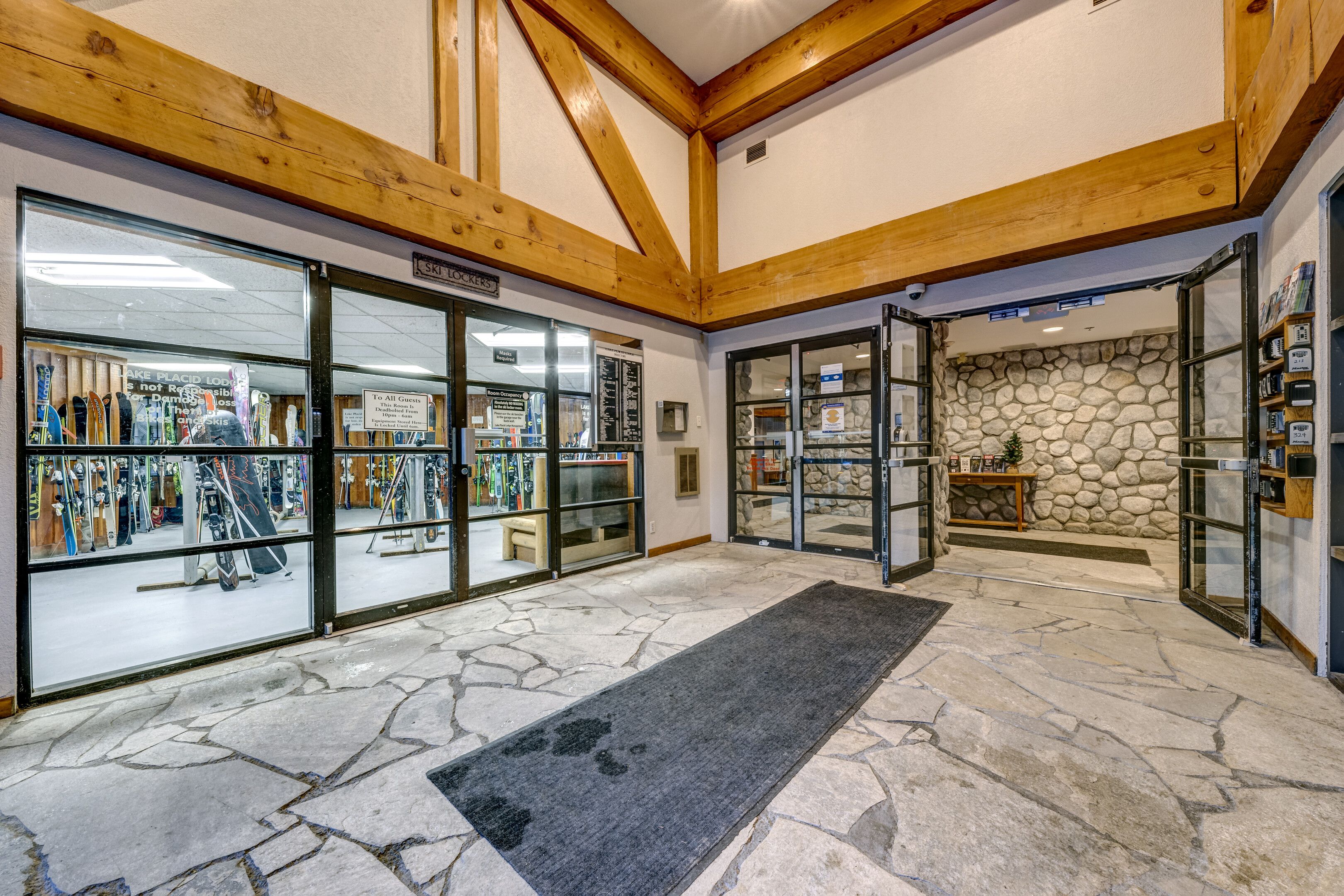 A ski lodge interior with wooden beams, a stone wall, and a ski equipment shop.