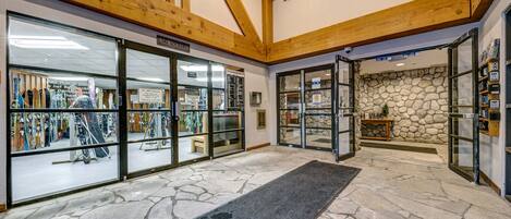 A ski lodge interior with wooden beams, a stone wall, and a ski equipment shop.