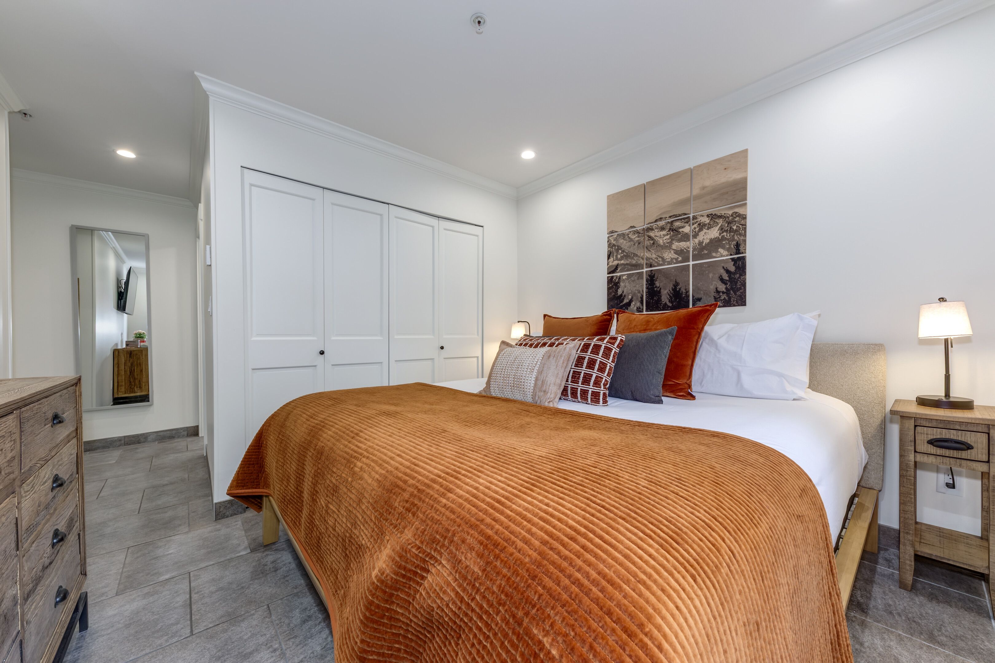 A bedroom with a large bed, a wardrobe, a bedside table, and a wall-mounted artwork.