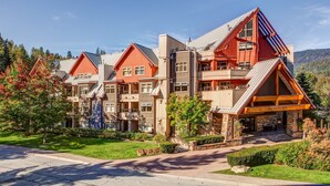 A multi-story lodge with a prominent red and beige color scheme, featuring a large entrance with a covered porch and stone accents. - Lake Placid Lodge - Ski-In/Out, Pool, Hot Tub & Sauna, No Stairs (Whistler)