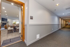 A hallway with a carpeted floor, a door with a number sign, and a view into a dining area with a table and chairs. - Lake Placid Lodge 126 (Whistler)