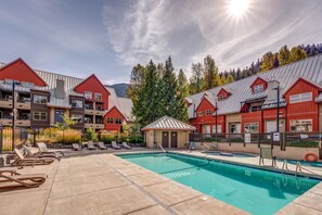 A pool area with lounge chairs and a small building, surrounded by red and grey buildings with a mountainous backdrop.