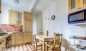 A kitchen with wooden cabinets, a dining table with chairs, a microwave, and a clock on the wall. - Reflets d'Argent- Cosy & Soft - by Mon Petit Faré (Paris)