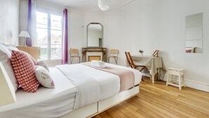 Un dormitorio con cama, escritorio, silla, espejo y ventana con cortinas.