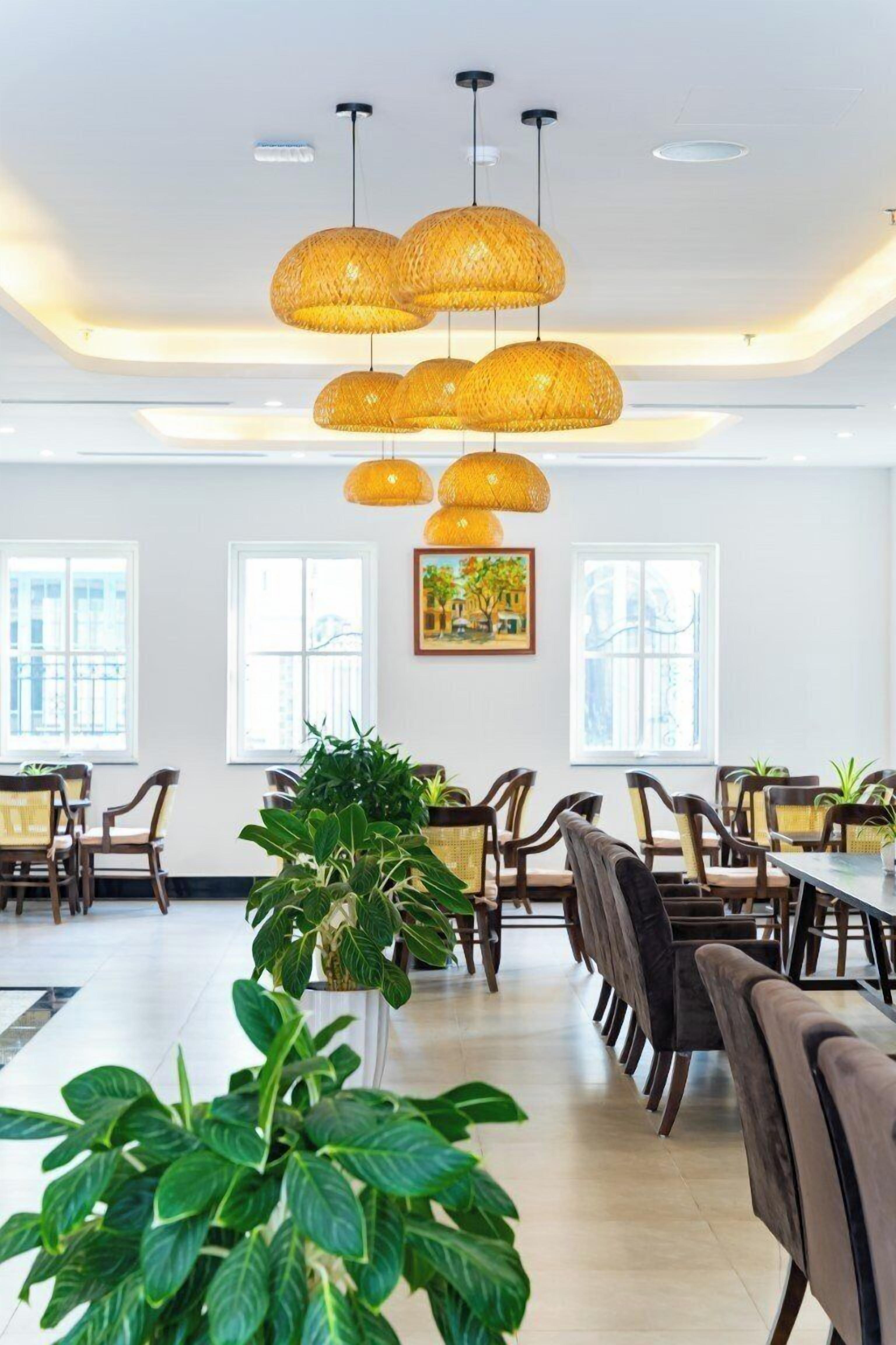 A spacious dining area with multiple tables and chairs, large windows, and hanging wicker pendant lights.