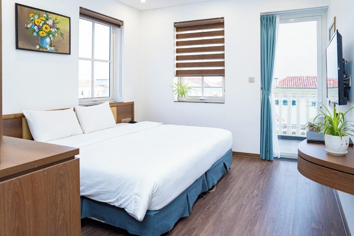 A hotel room with a bed, a desk, a TV, and a window with a view of buildings.