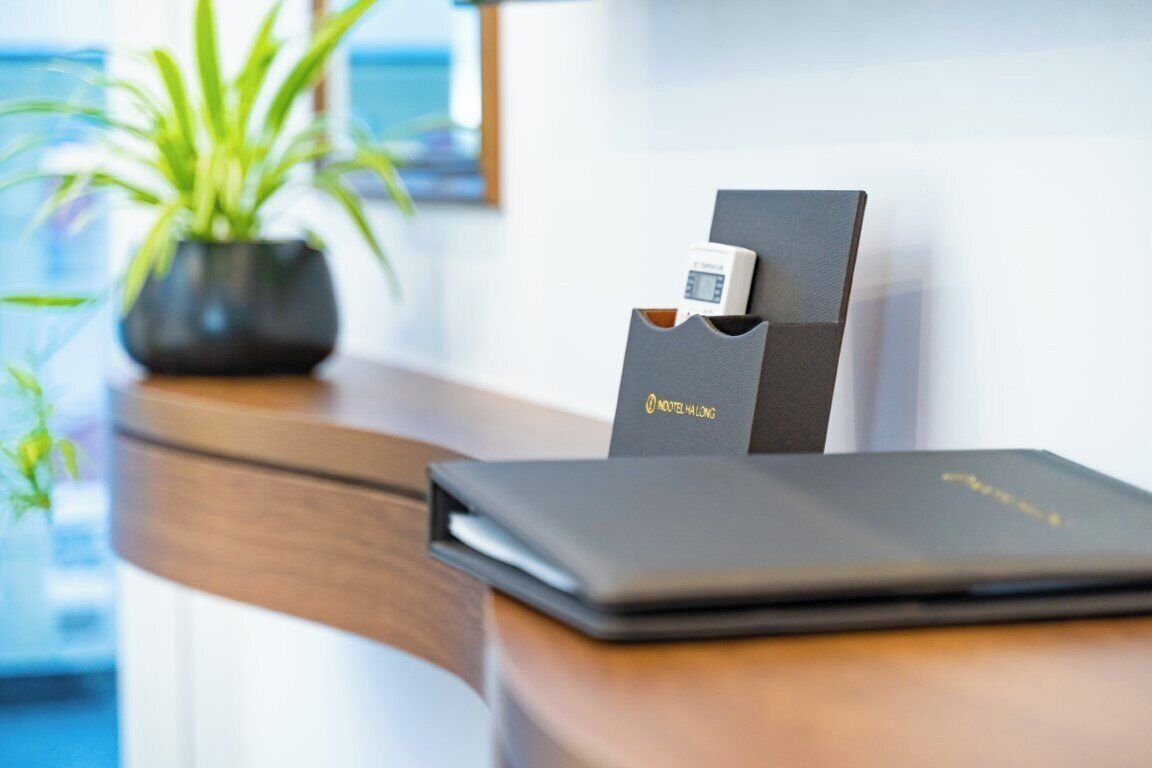 A wooden reception desk with a laptop, a digital clock, and a sign reading "Noodle Halong".