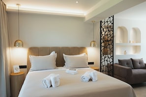 A hotel room with a large bed, two bedside tables, a grey sofa, a decorative wall panel, and two pendant lights.