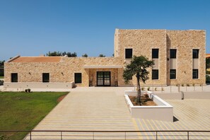 A modern building with a stone facade, a central entrance, and a paved courtyard.