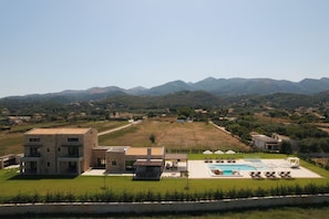 A modern villa with a swimming pool, outdoor seating, and a view of the surrounding hills.