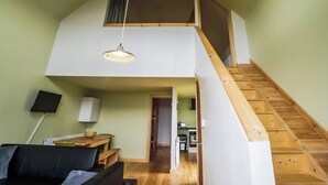 A loft-style room with a wooden staircase, a dining area, and a living space with a sofa and a TV.