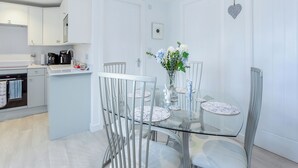 Une cuisine moderne avec des meubles blancs, une machine à café et un coin repas comprenant une table en verre et des chaises blanches.