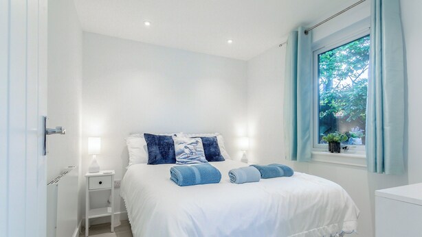 Une chambre à coucher avec un lit, des tables de chevet, une fenêtre avec des rideaux et une vue sur la verdure à l’extérieur.