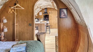 A cozy, wooden interior with a kitchen area visible through an archway, a hanging rack, and a framed picture on the wall.