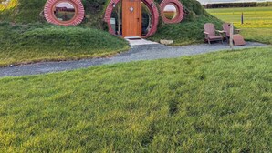A circular building with a wooden door and windows, surrounded by grass and a gravel path.