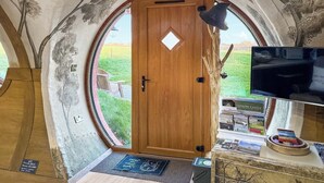 A room with a wooden door, a round window, a television, and a small table with magazines.