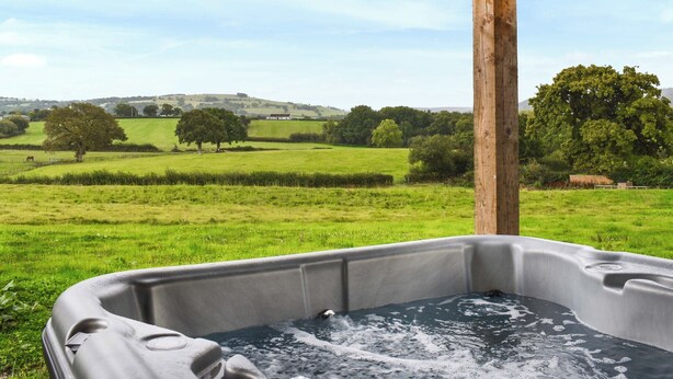 Un jacuzzi bajo una pérgola de madera con vistas a un campo verde y árboles.