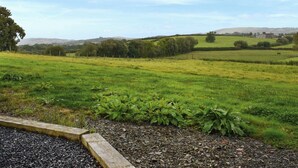 Un paisaje rural con un campo cubierto de hierba, un muro de piedra y una casa a lo lejos.