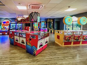 A variety of arcade games in a brightly lit indoor space with wooden flooring.