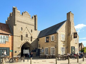 A historic building with a prominent tower and arched entrance, featuring outdoor seating and directional signs for local attractions. - 1 bedroom accommodation in Filey (Filey)