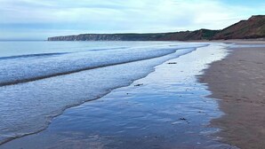 A beach with a calm sea, a sandy shore, and a cliff in the background. - 1 bedroom accommodation in Filey (Filey)