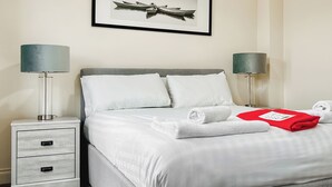 A neatly made bed with white linens, two bedside tables with lamps, a framed picture on the wall, and a red towel on the bed. - 1 bedroom accommodation in Filey (Filey)