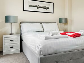 A neatly made bed with white linens, two bedside tables with lamps, a framed picture on the wall, and a red towel on the bed.