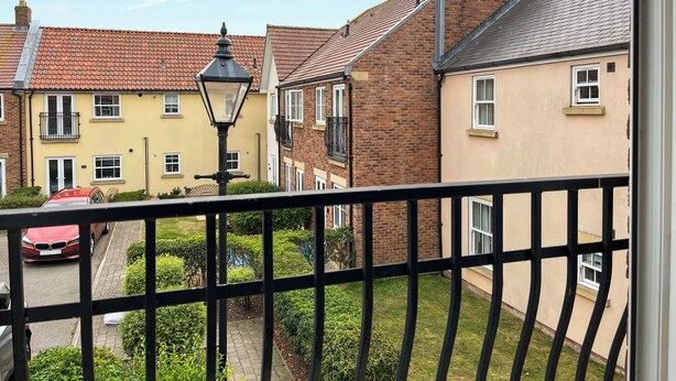 A residential street with houses, a red car, and a black metal fence. - 1 bedroom accommodation in Filey (Filey)
