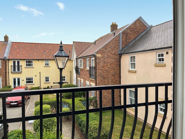 A residential street with houses, a red car, and a black metal fence. - 1 bedroom accommodation in Filey (Filey)
