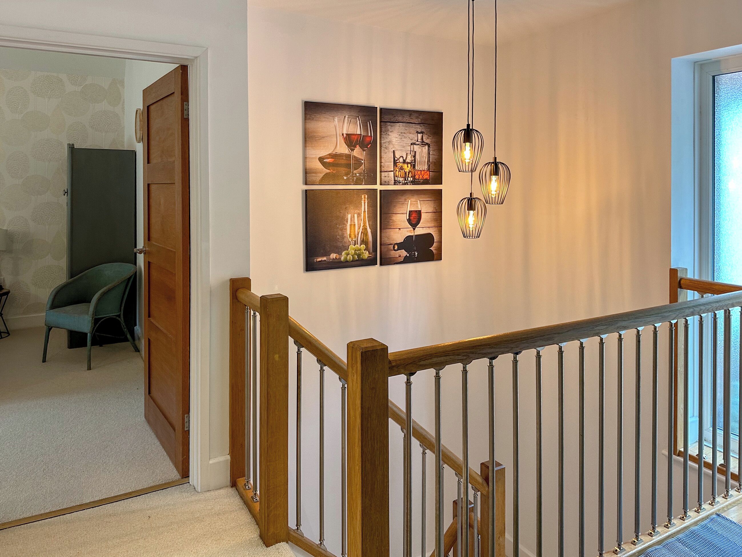 A staircase with a wooden handrail and metal balusters, leading to a landing with a wall-mounted light fixture and framed artwork.