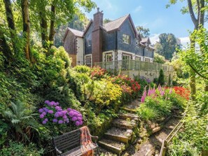 A large house surrounded by lush gardens and a wooden bench. - 4 bedroom accommodation in Lynton (Lynton)