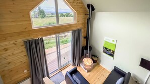 A room with a sloped wooden ceiling, a large window with curtains, a fireplace, and a sofa. - Glamping made easy near Kielder: eco design, family fun, and endless stars. (Hexham, near Bellingham)