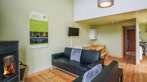 A cozy living room with a fireplace, a sofa, a wooden dining table, and a television. - Glamping made easy near Kielder: eco design, family fun, and endless stars. (Hexham, near Bellingham)
