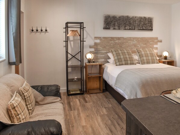 Une chambre à coucher avec un lit, une table de chevet, un plancher en bois, une étagère fixée au mur et une fenêtre avec des rideaux.