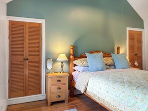 Un dormitorio con cama, mesita de noche con lámpara, espejo y dos puertas de madera.