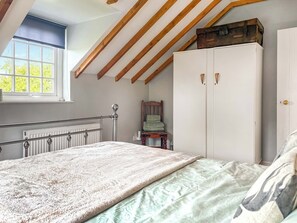 Un dormitorio con techo inclinado, un radiador, una cama con colcha estampada, un banco de madera y un armario con dos puertas.